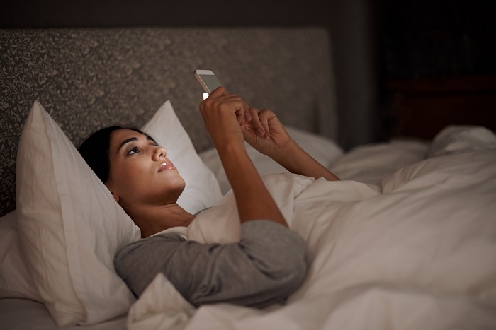 A young woman sending a text message while in bed.