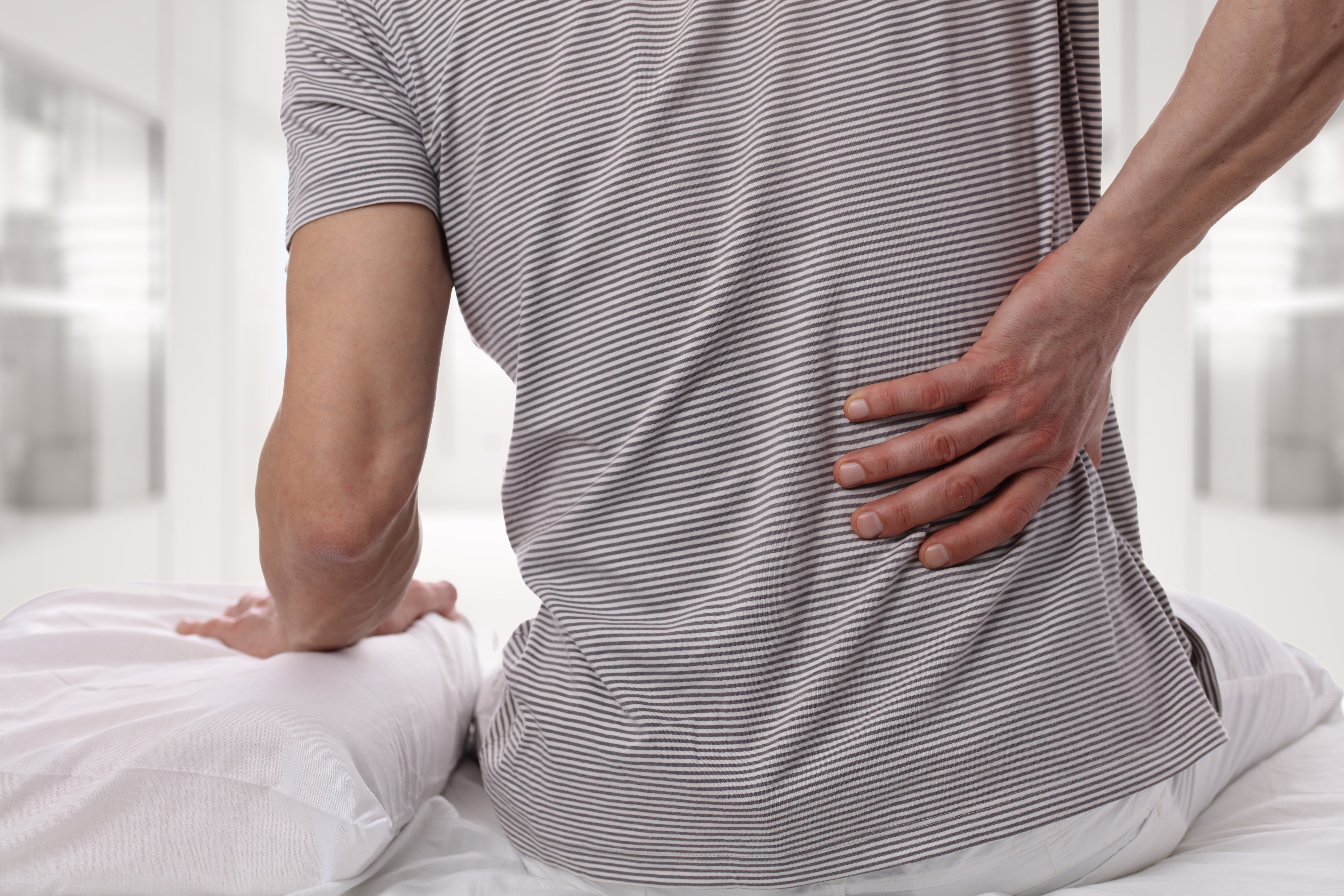 Man grabbing his lower back while sitting up in bed 