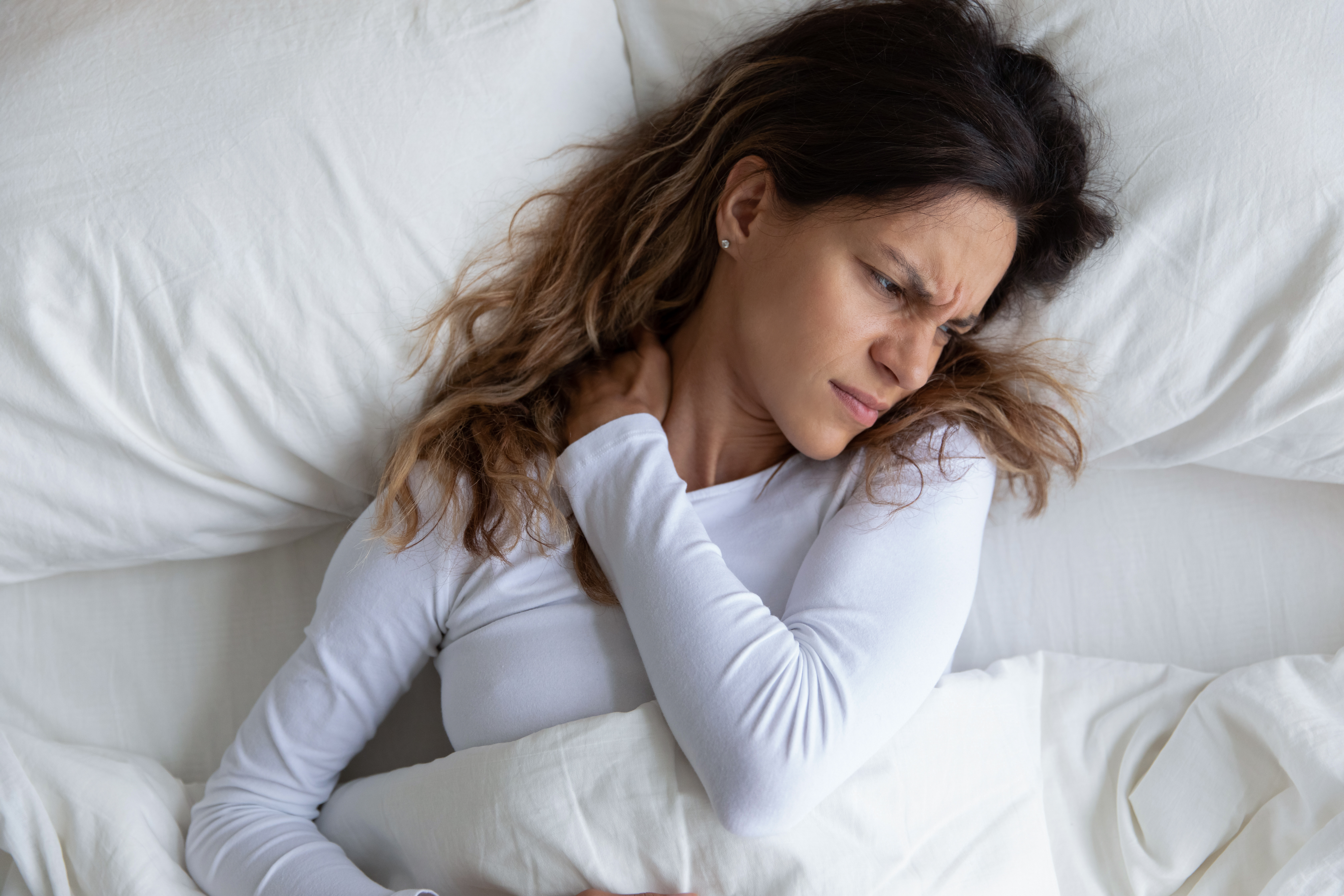 Woman grabs her shoulders in pain while lying in bed