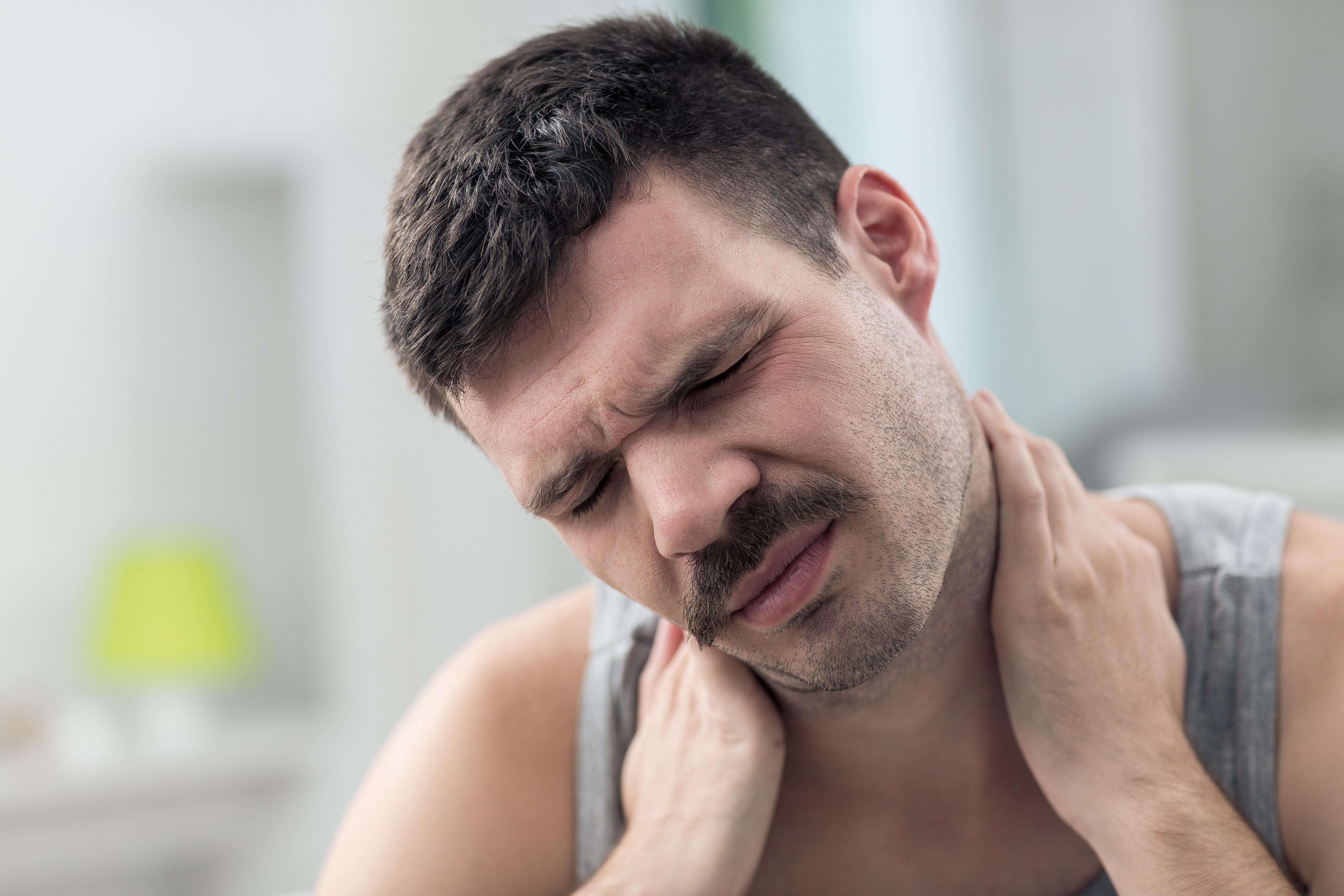 A man wincing while grabbing his neck 