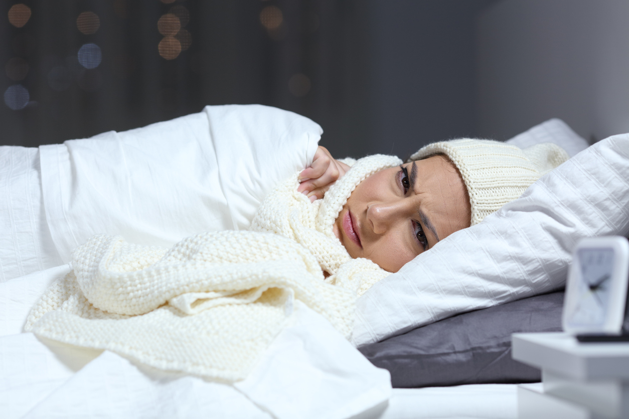 cold woman bundles up with blankets and a hat in bed