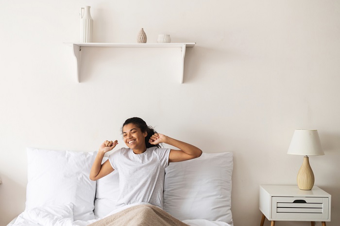 Joyful woman with dark hair sitting in bed stretching and smiling. 