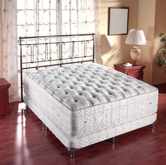 Innerspring mattress with metal bedframe sitting in a modern bedroom with red hardwood flooring. 