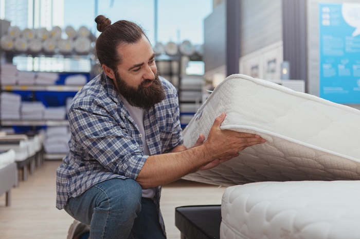 Bearded man examining an innerspring mattress at a furnishings store.