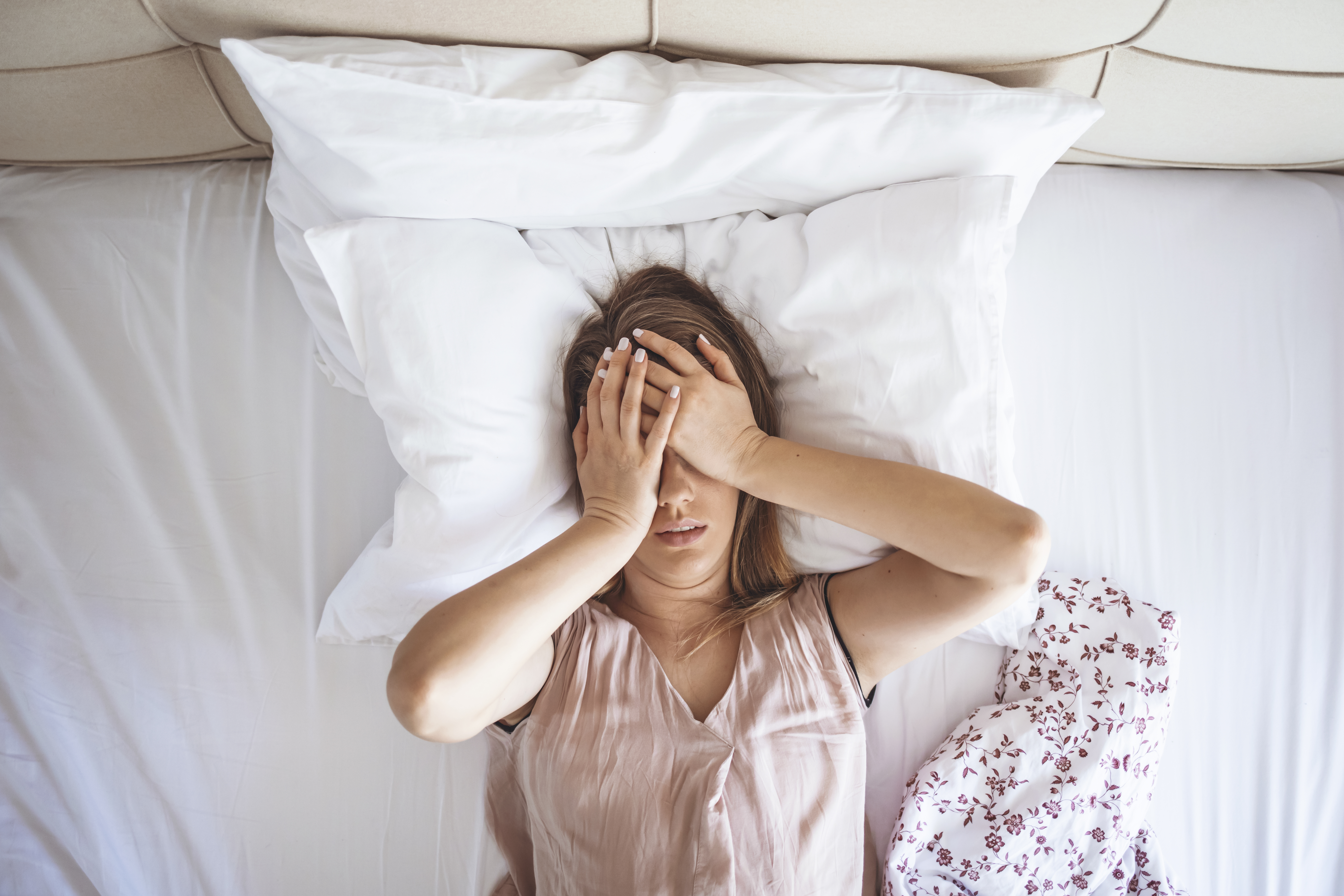 A woman grabbing her face in fatigue while in bed 