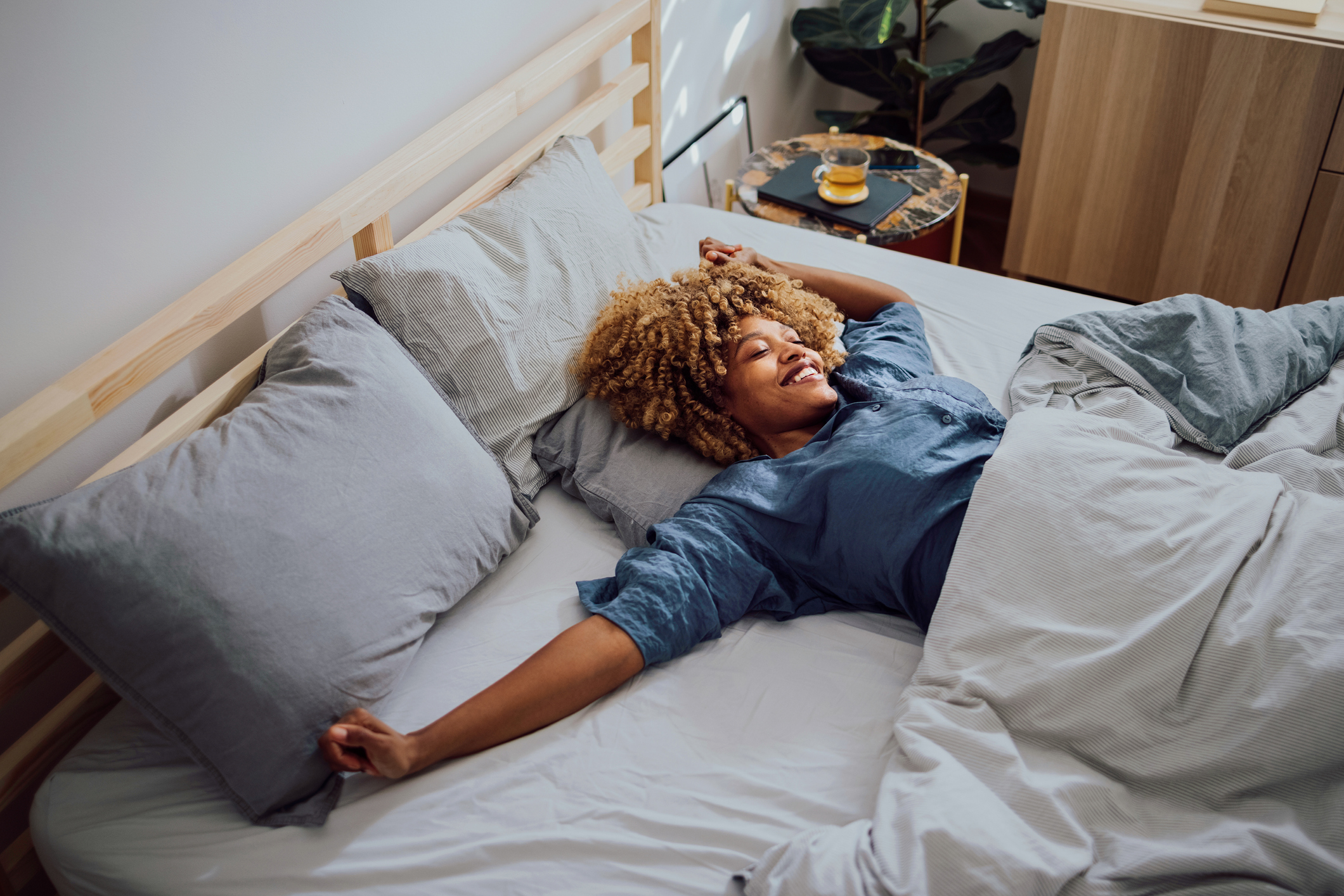 A woman in blue pajamas smiling and stretching in bed 