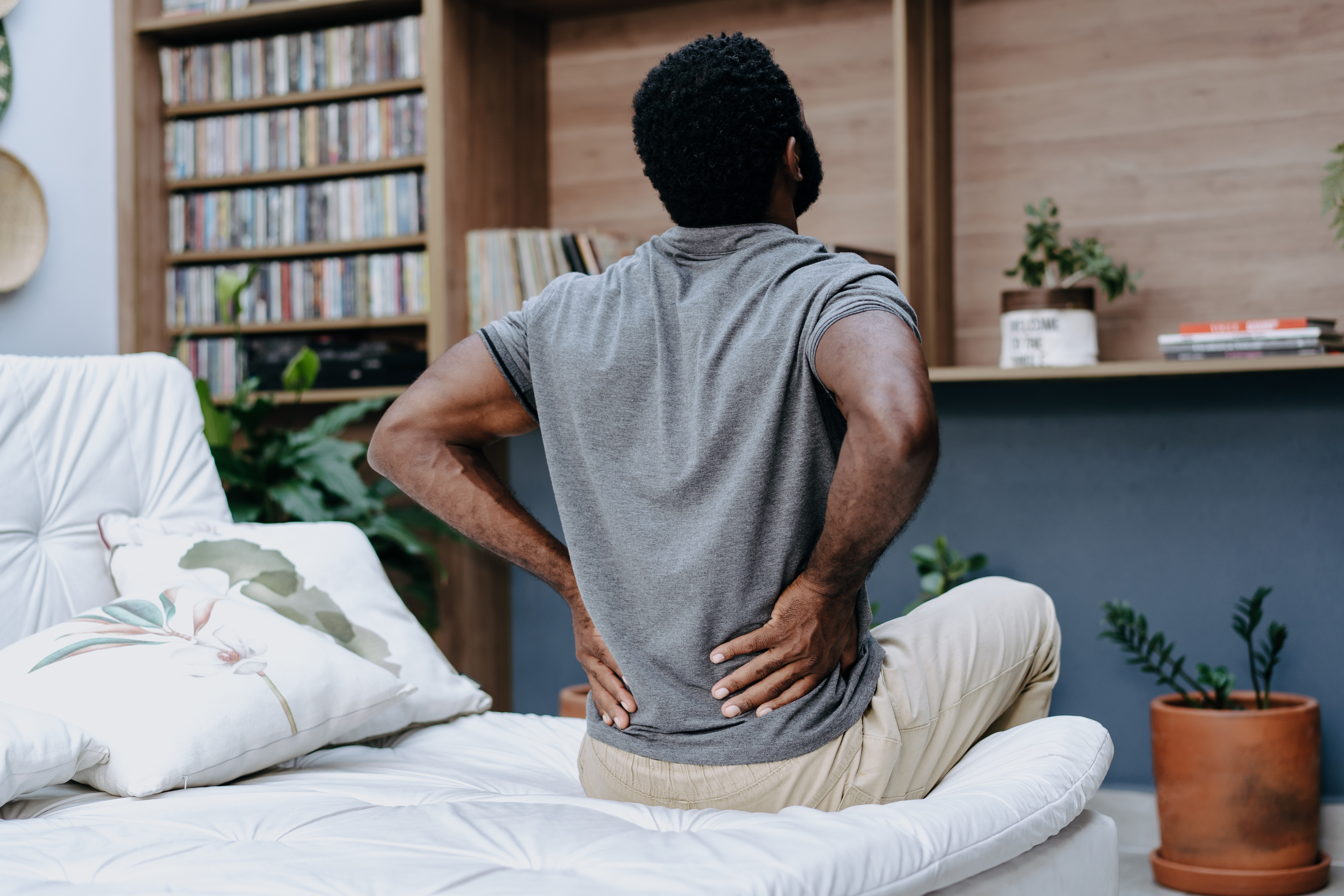 A man sitting up in a bed holding his back 