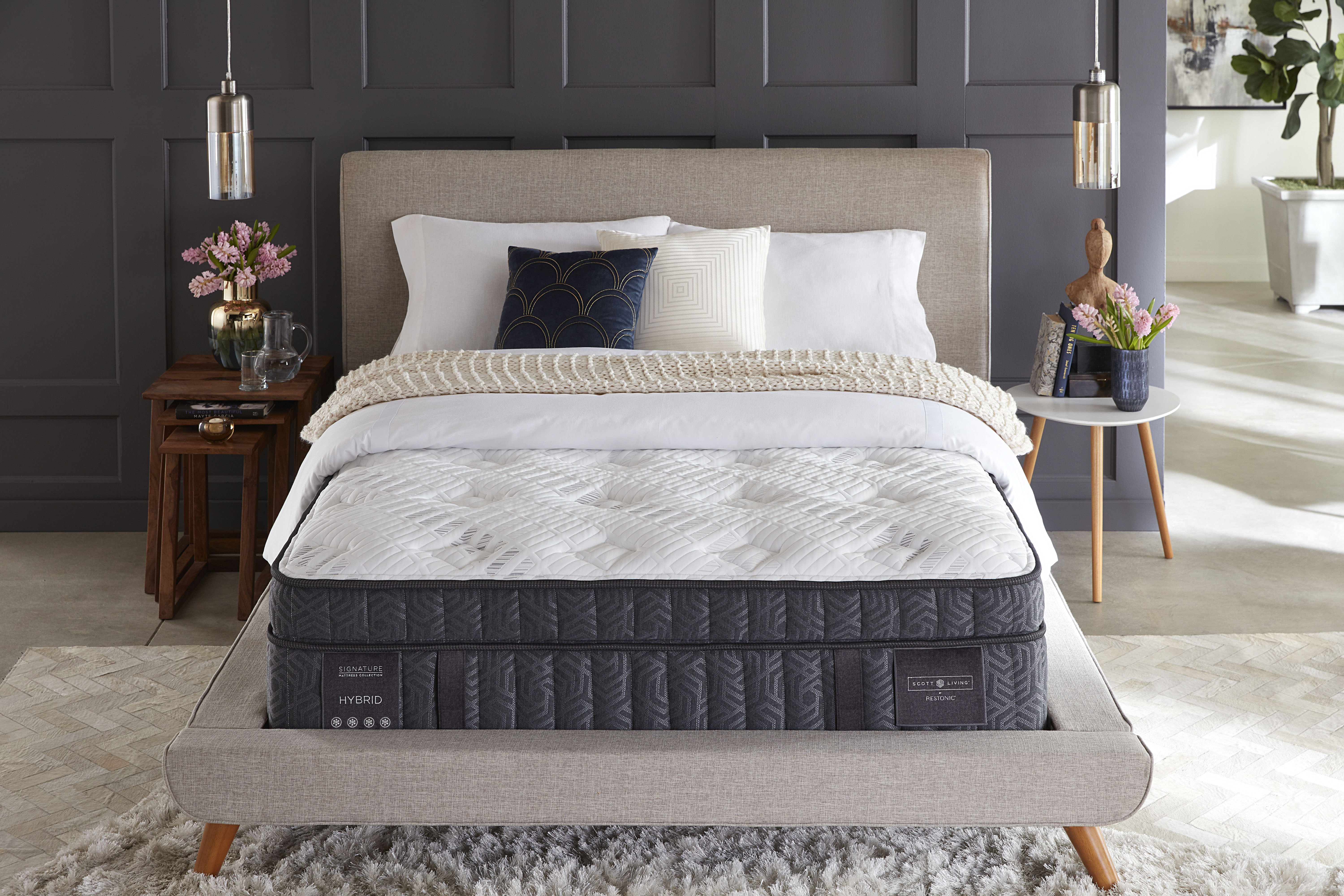 Scott Living mattress sits atop an upholstered bed frame in a bedroom with dark, elegant walls
