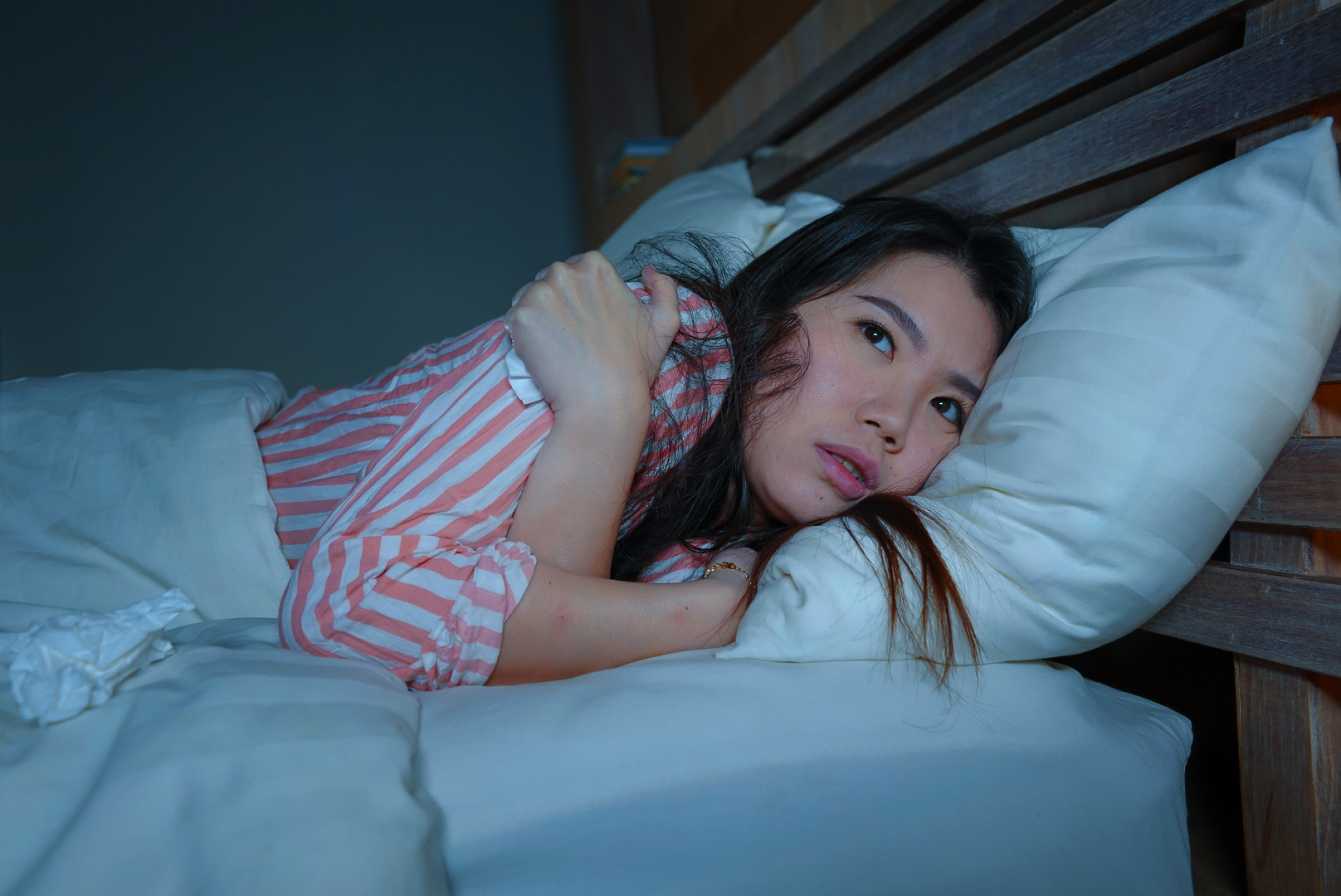 Young girl in striped shirt in bed cuddling herself from the cold 