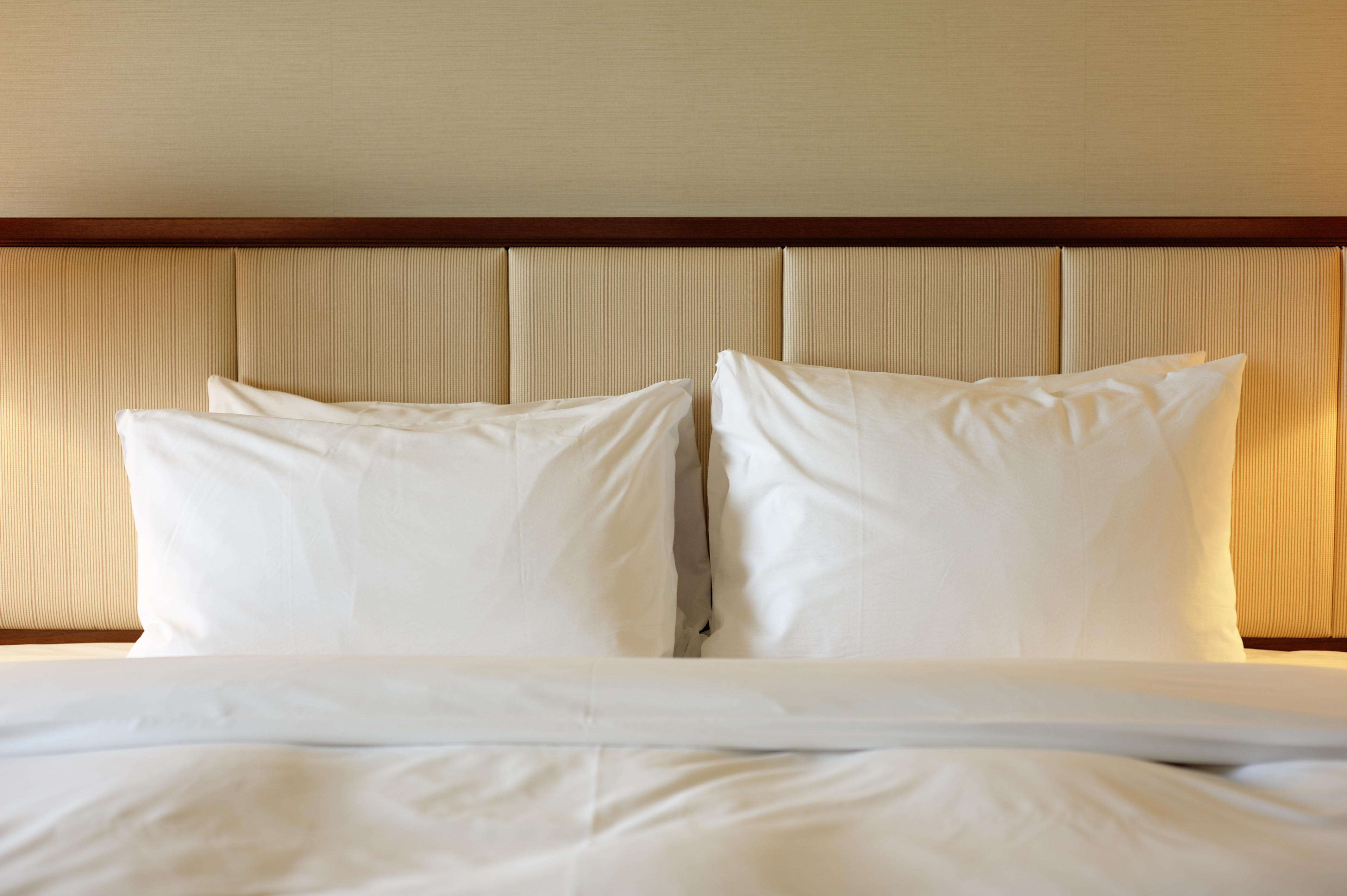 Close up of pillows neatly reclining against a channel tufted upholstered headboard 