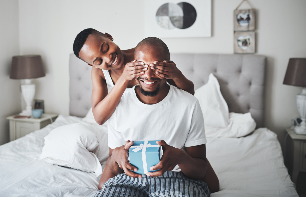 young woman surprises her husband with a gift in bed