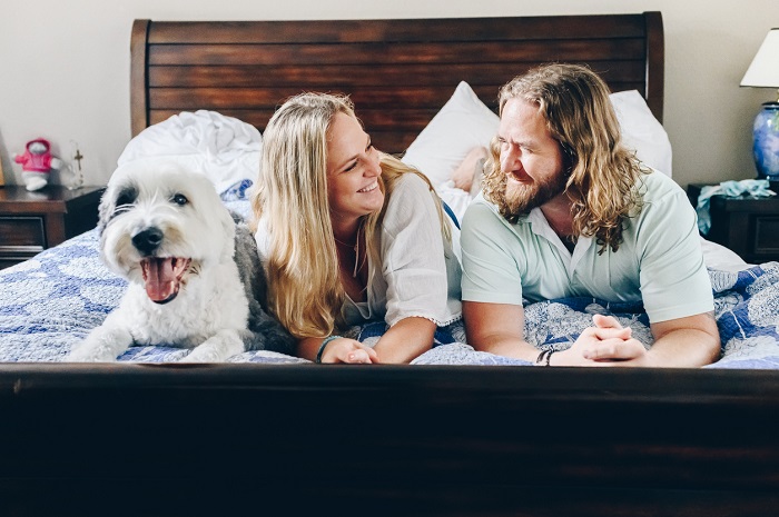Couple lying in bed at home in their bedroom happy and smiling with their dog.
