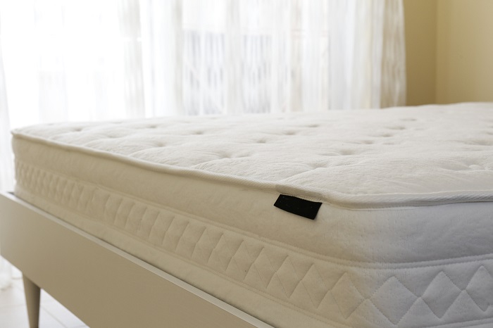 White orthopedic mattress on an unmade bed in a bedroom.