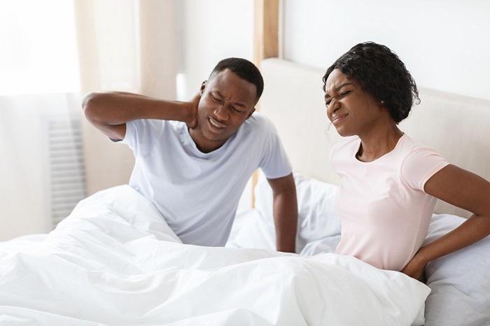 Young couple suffering from body pain after sleeping, touching their lower back and neck in bed. 