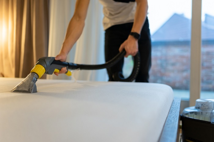 Man cleans bed from dirt and bacteria with a vacuum. 