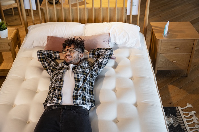 An adult man lying on a bed in a furniture store. 