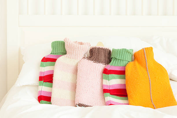 five hot water bottles in knitted covers on top of white linen