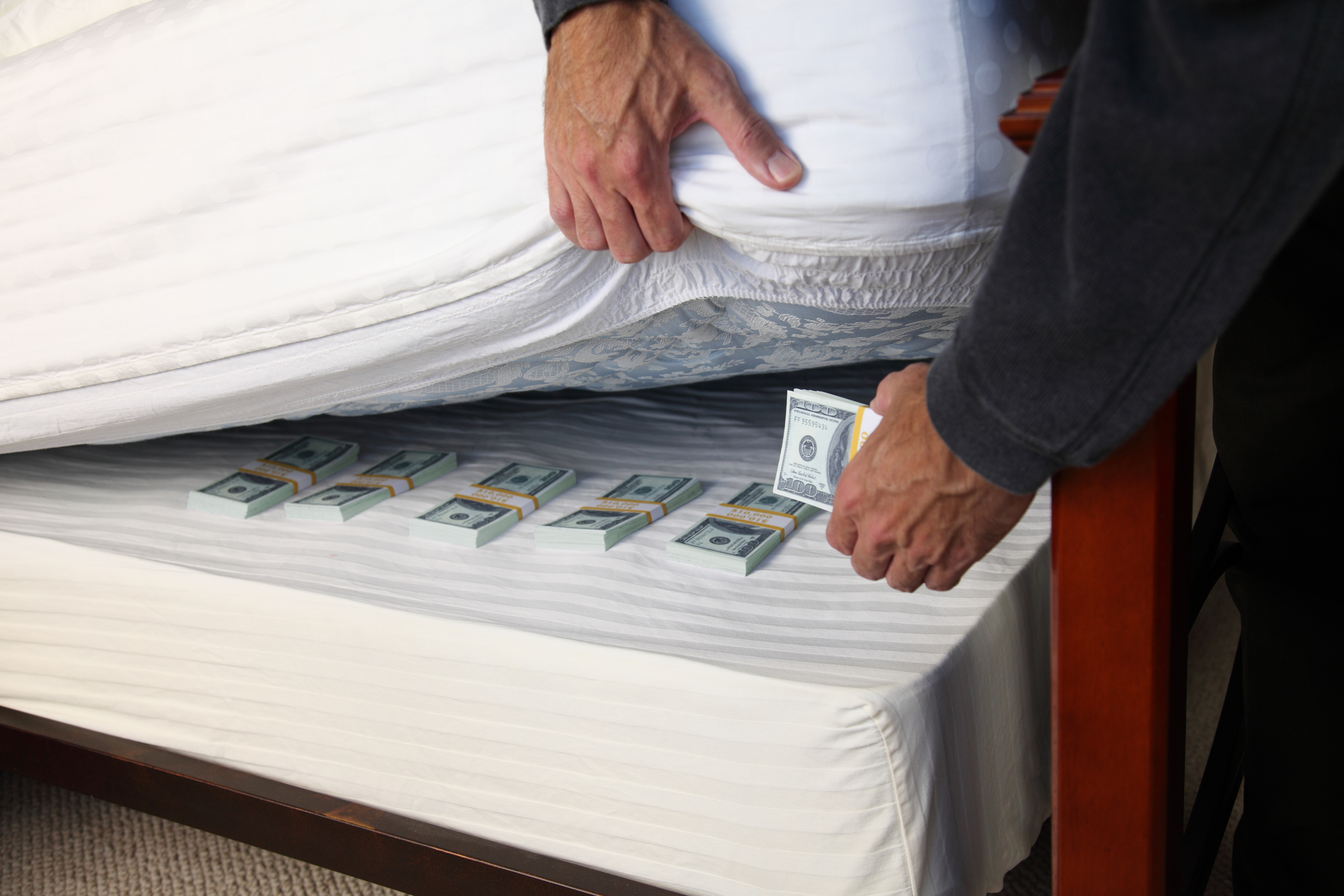 A person placing money underneath a mattress 