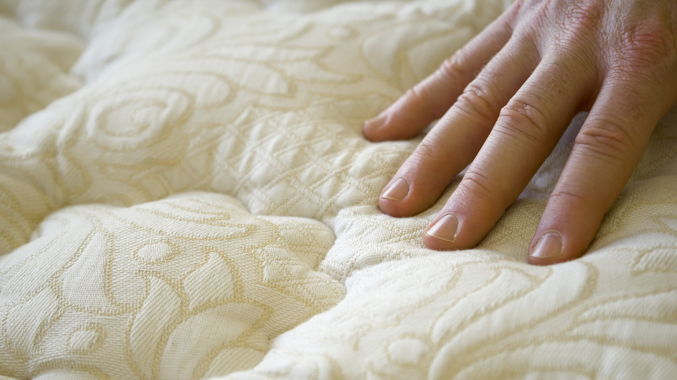 man touches to test the plushness of mattress before purchasing from store