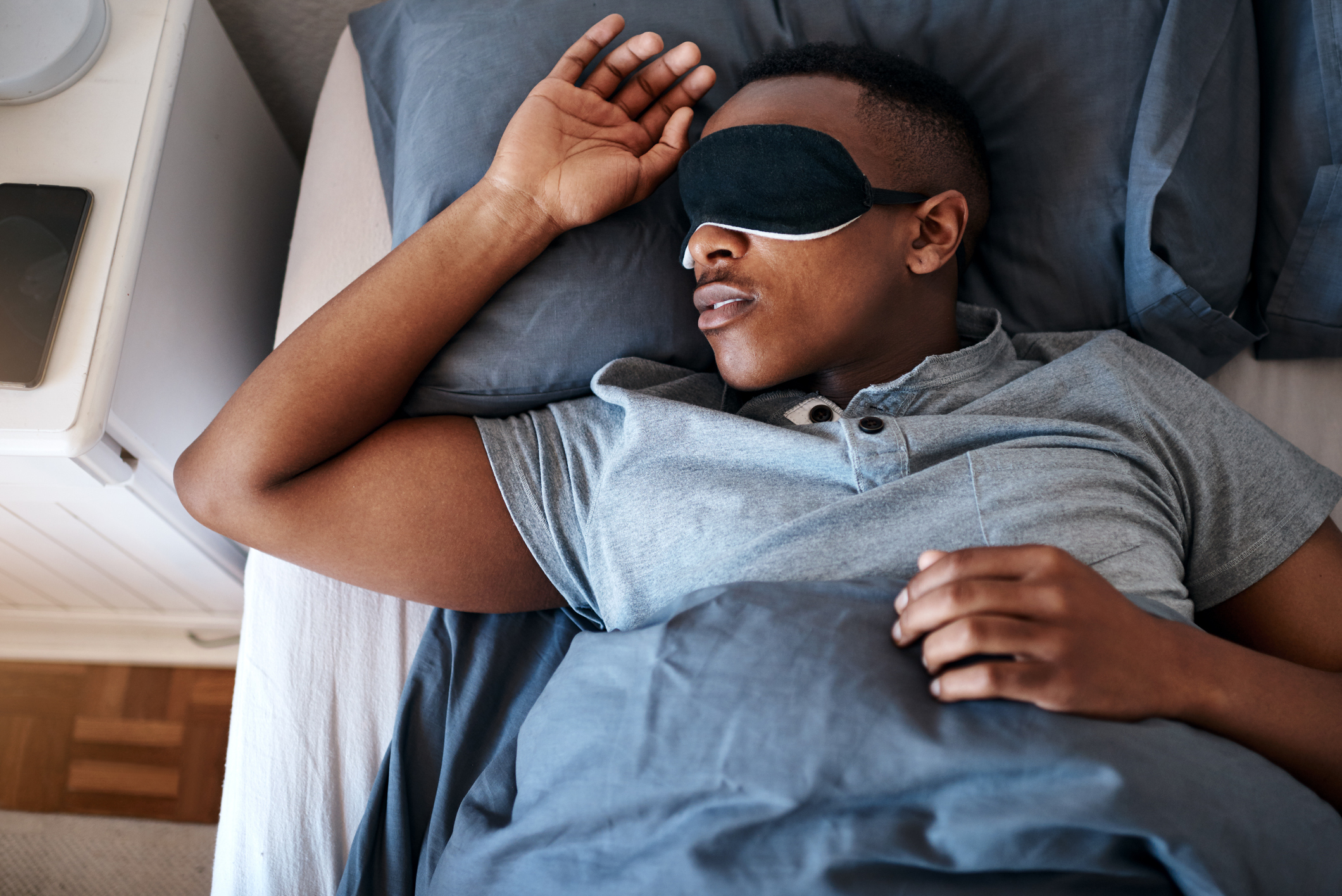 African American man in t shirt and sleep mask sleeping in bed