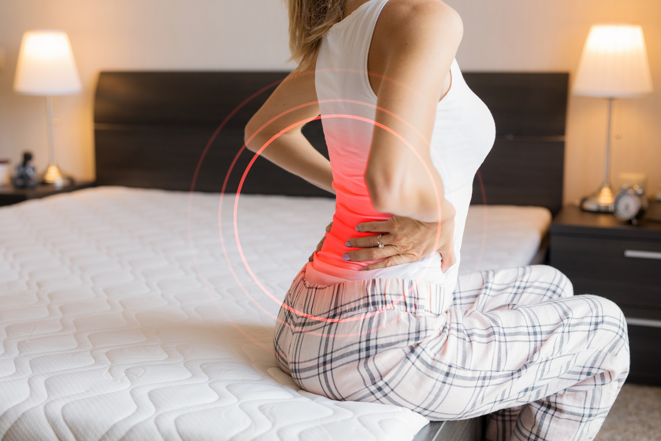 Woman sits on a bed and grabs back with graphic visual of pain 