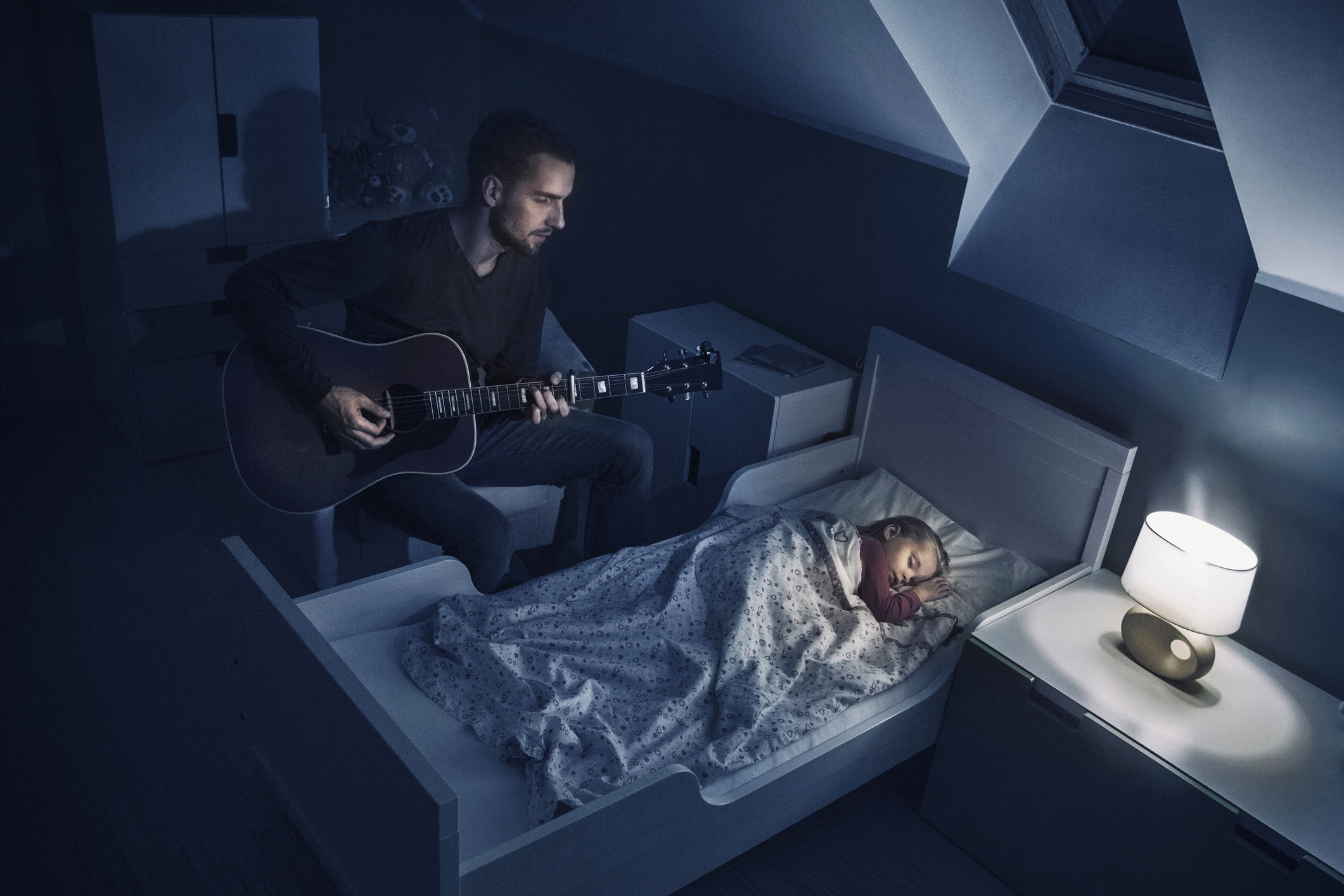 father playing the guitar, singing lullaby for his sleeping daughter