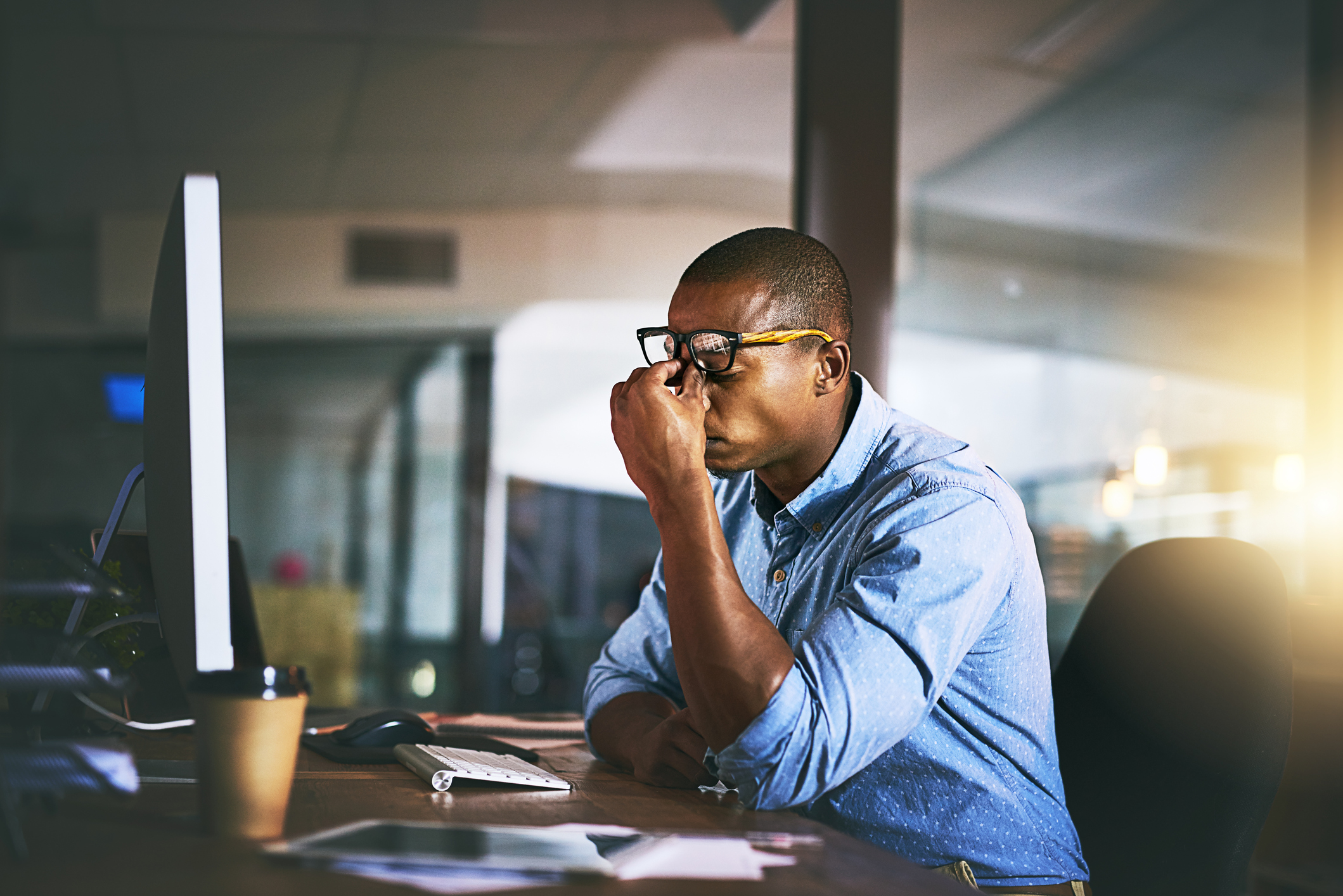  tired man rubbing his eyes while sitting at his desk at work