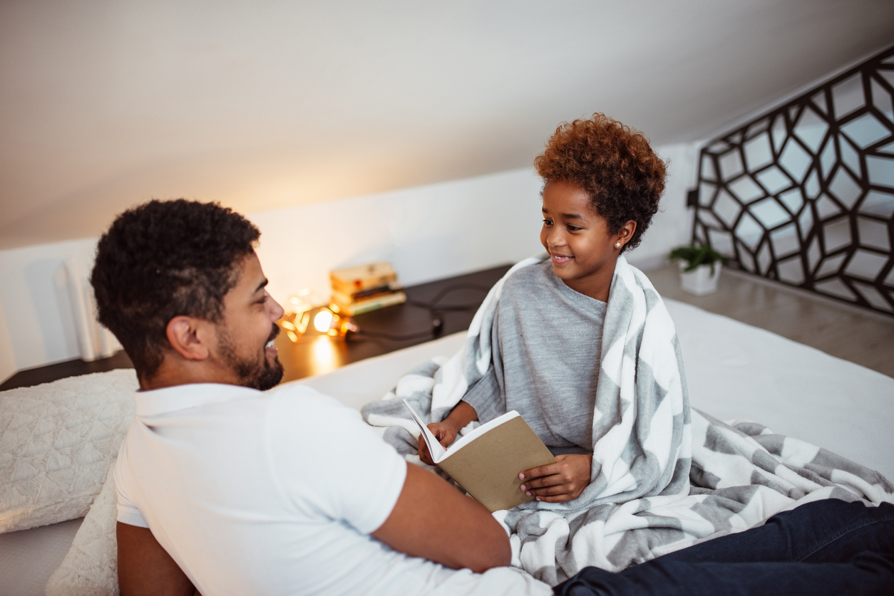 Dad and his daughter read together in bed