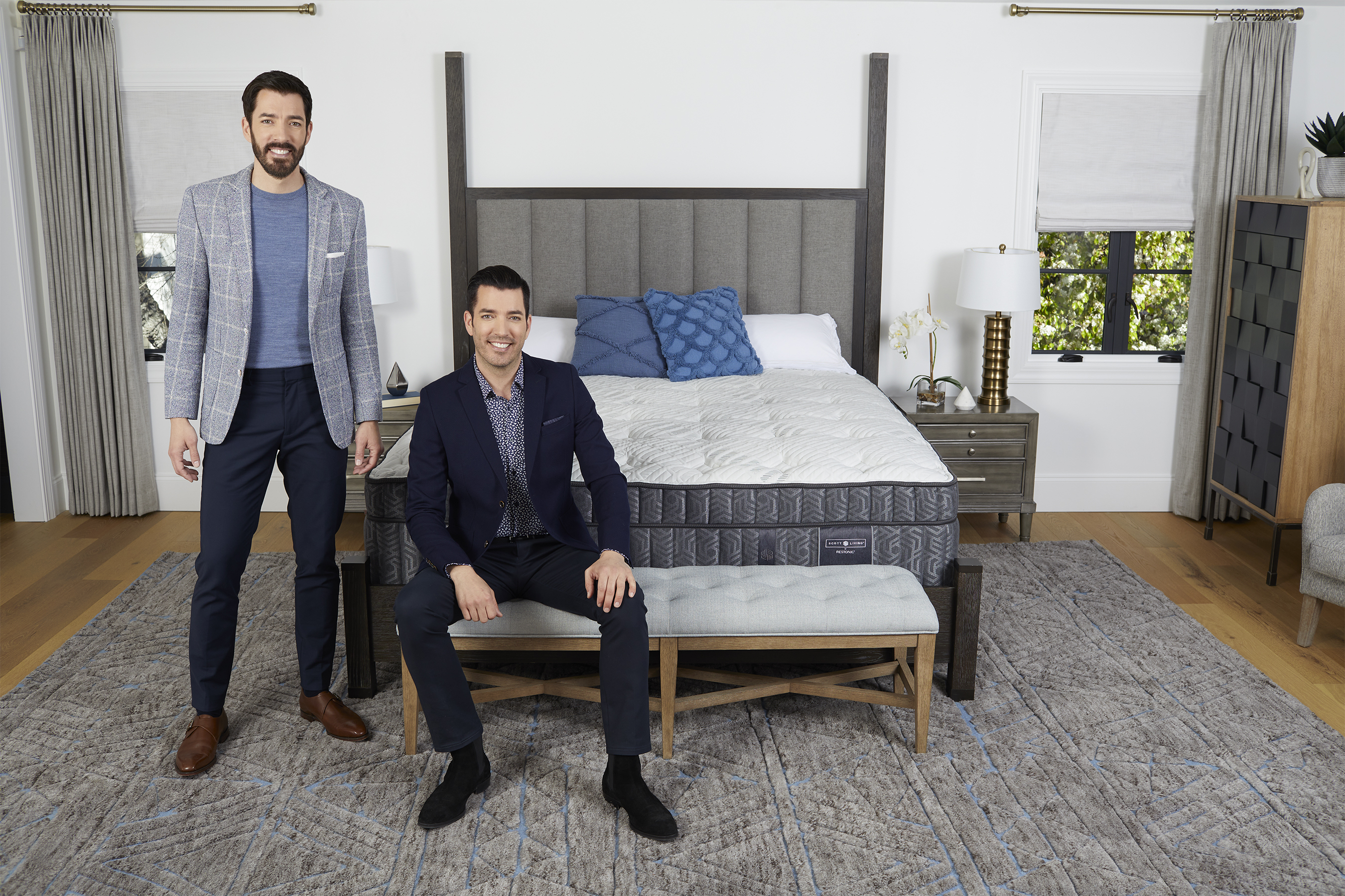 Drew & Jonathan Scott sit on and stand beside one of the mattresses from their collection.