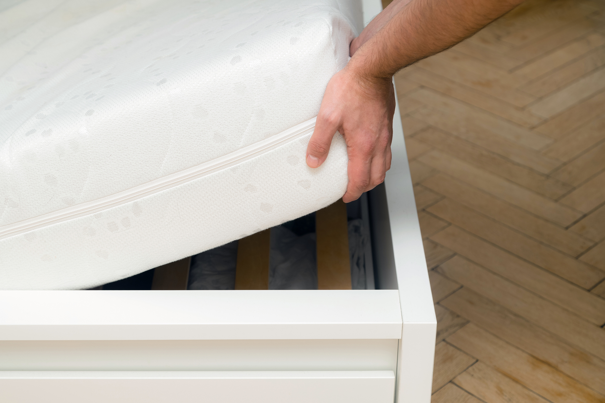 User slipping a mattress into a wooden bed frame
