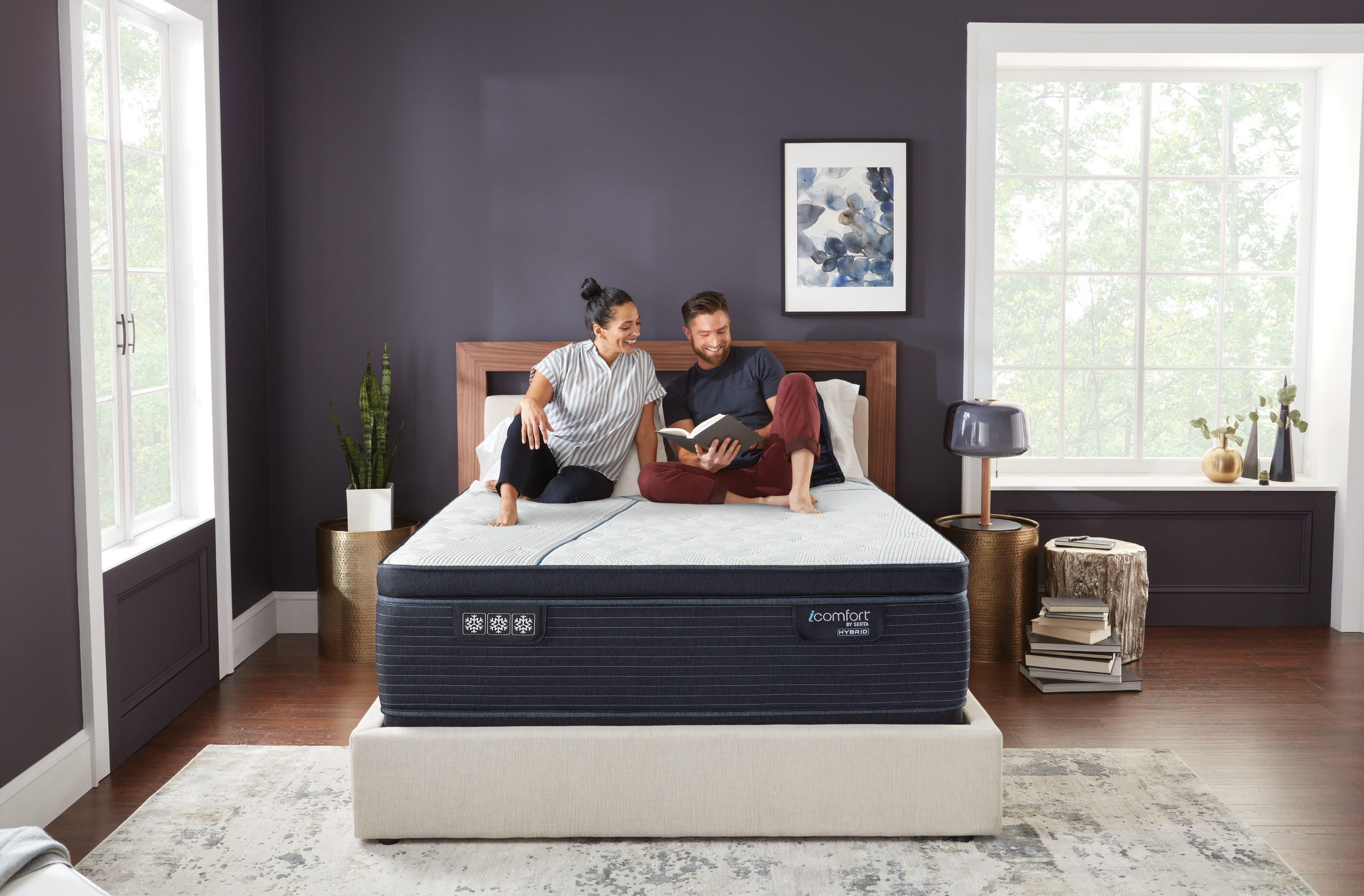 couple sitting on their Serta mattress looking at a book