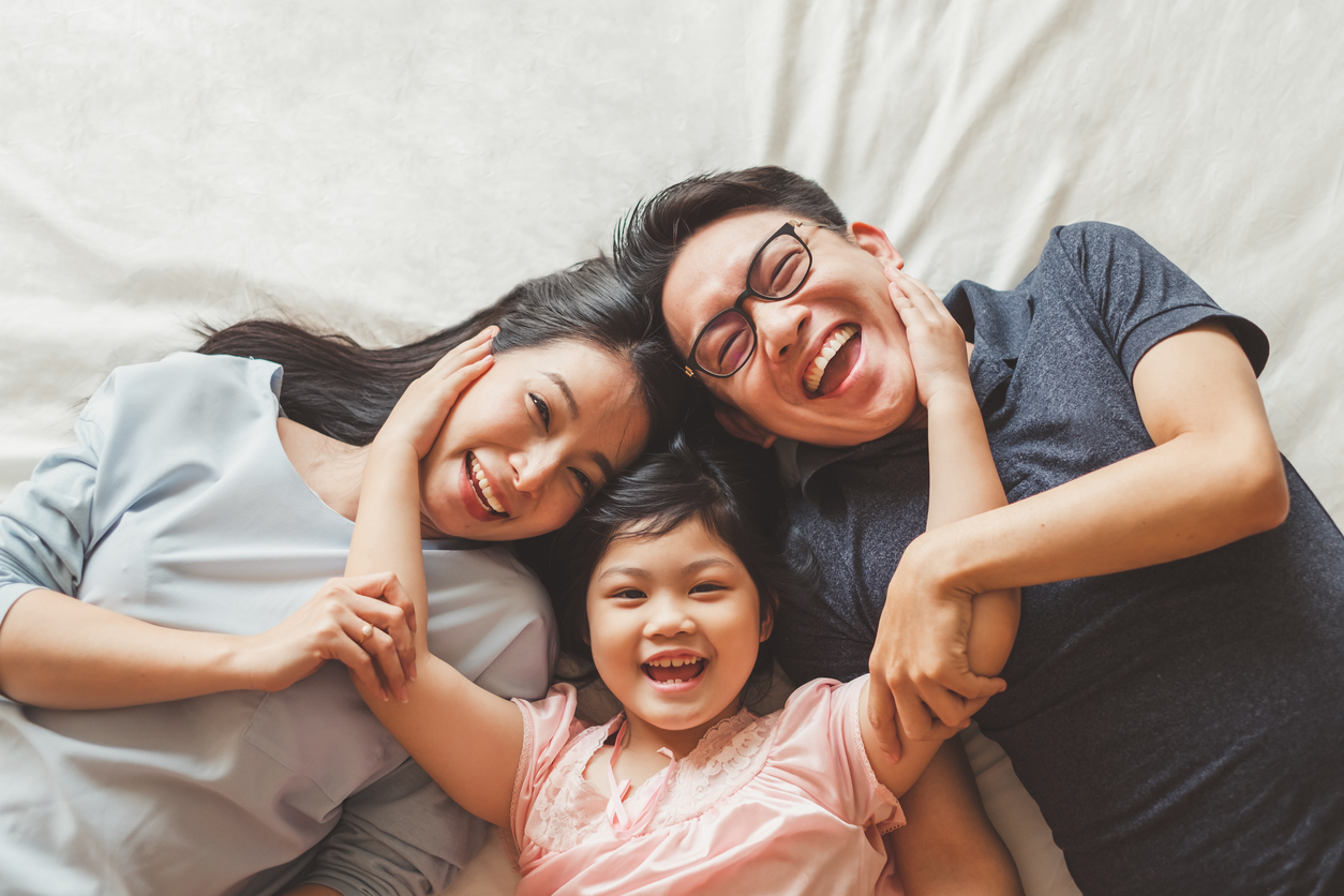 smiling mother and father pose lie in bed with daughter between them