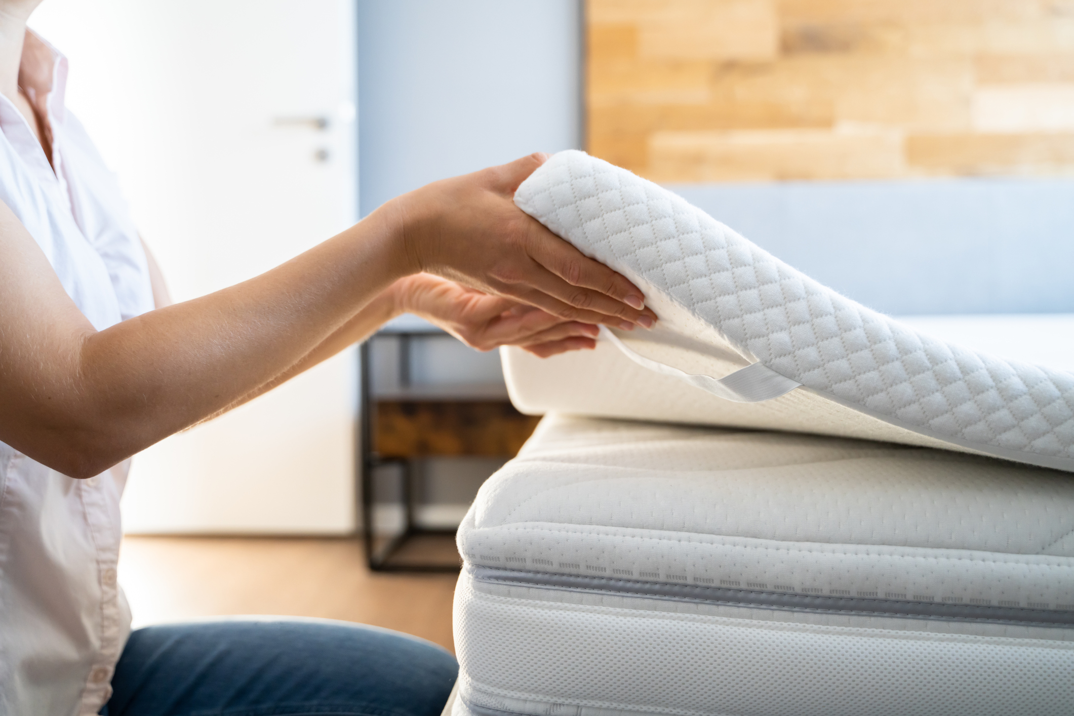 A woman placing a memory foam mattress topper on a mattress 