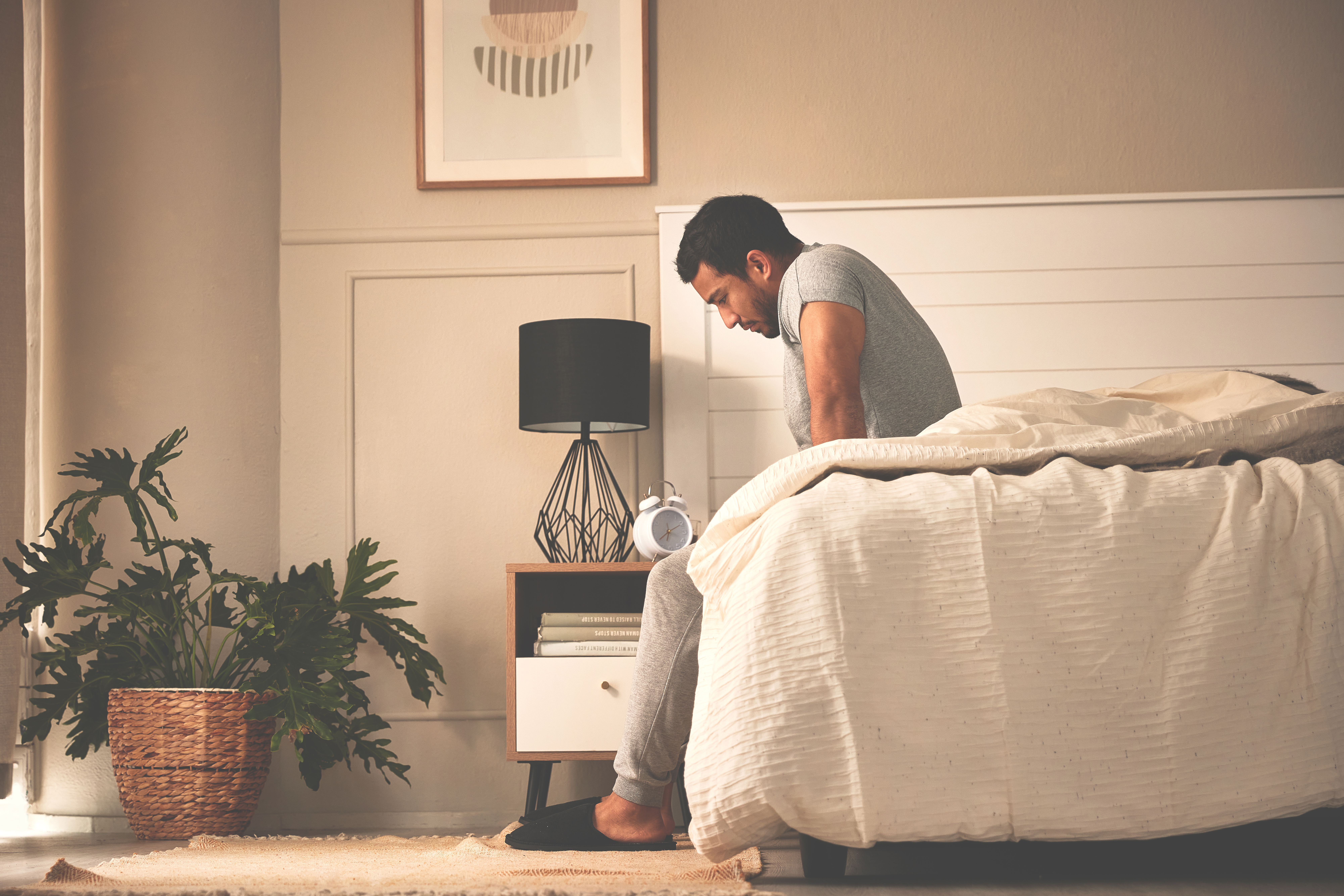 A young man sitting on the edge of the bed in pain 