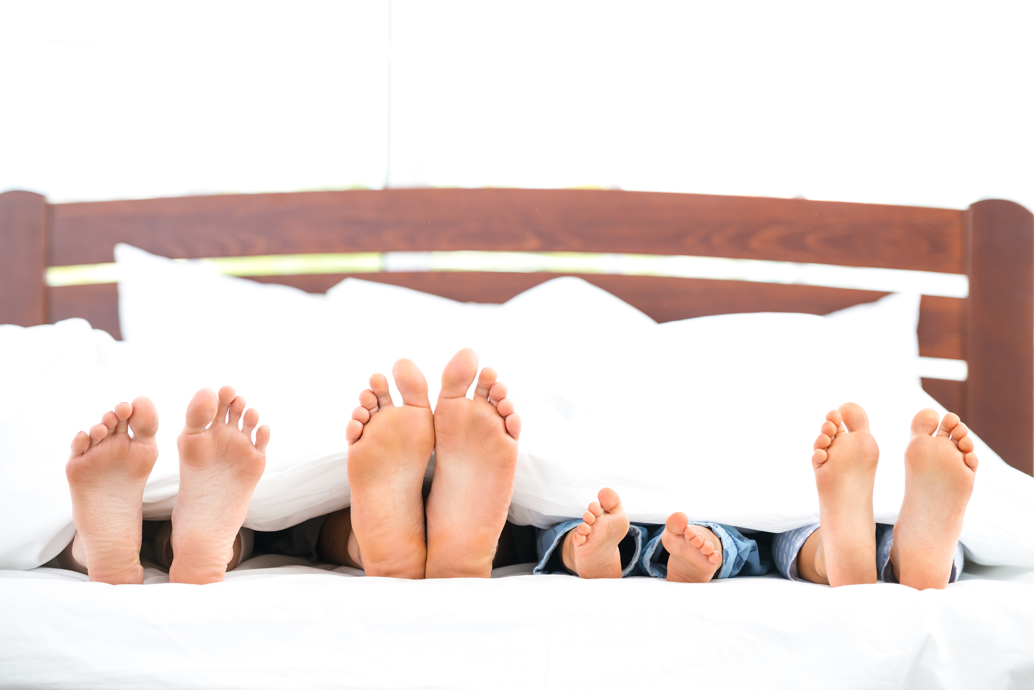 a family on a mattress sticks their feet out from a white comforter