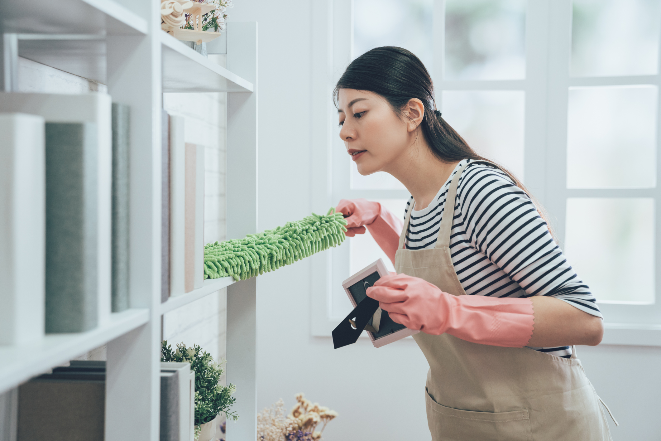 woman dusting behind the bookshelves 
