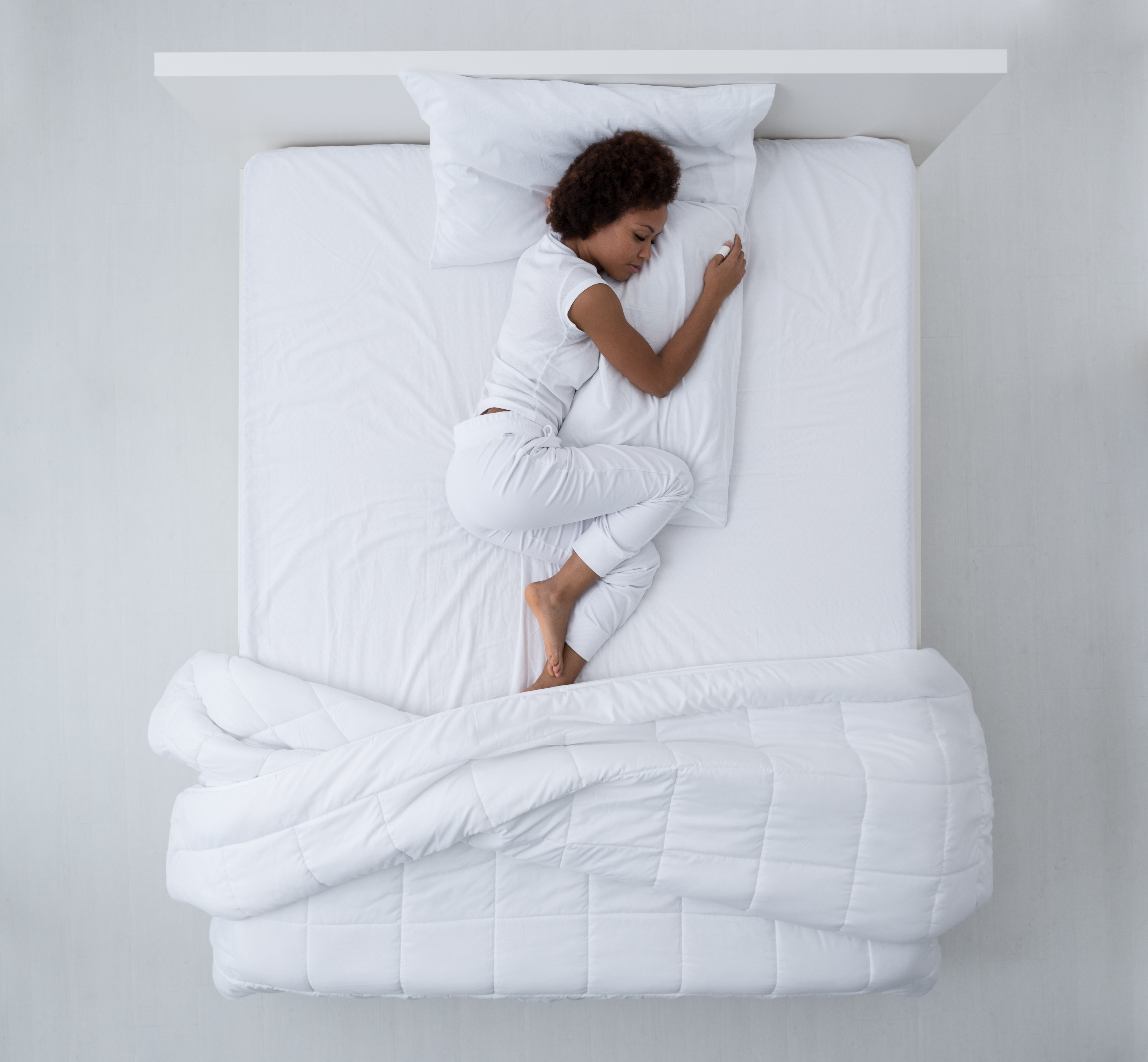 A young woman in white pajamas sleeping on a bed with white bedding 