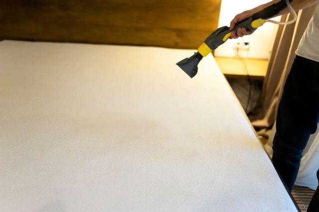 view of a person holding a vacuum over a mattress