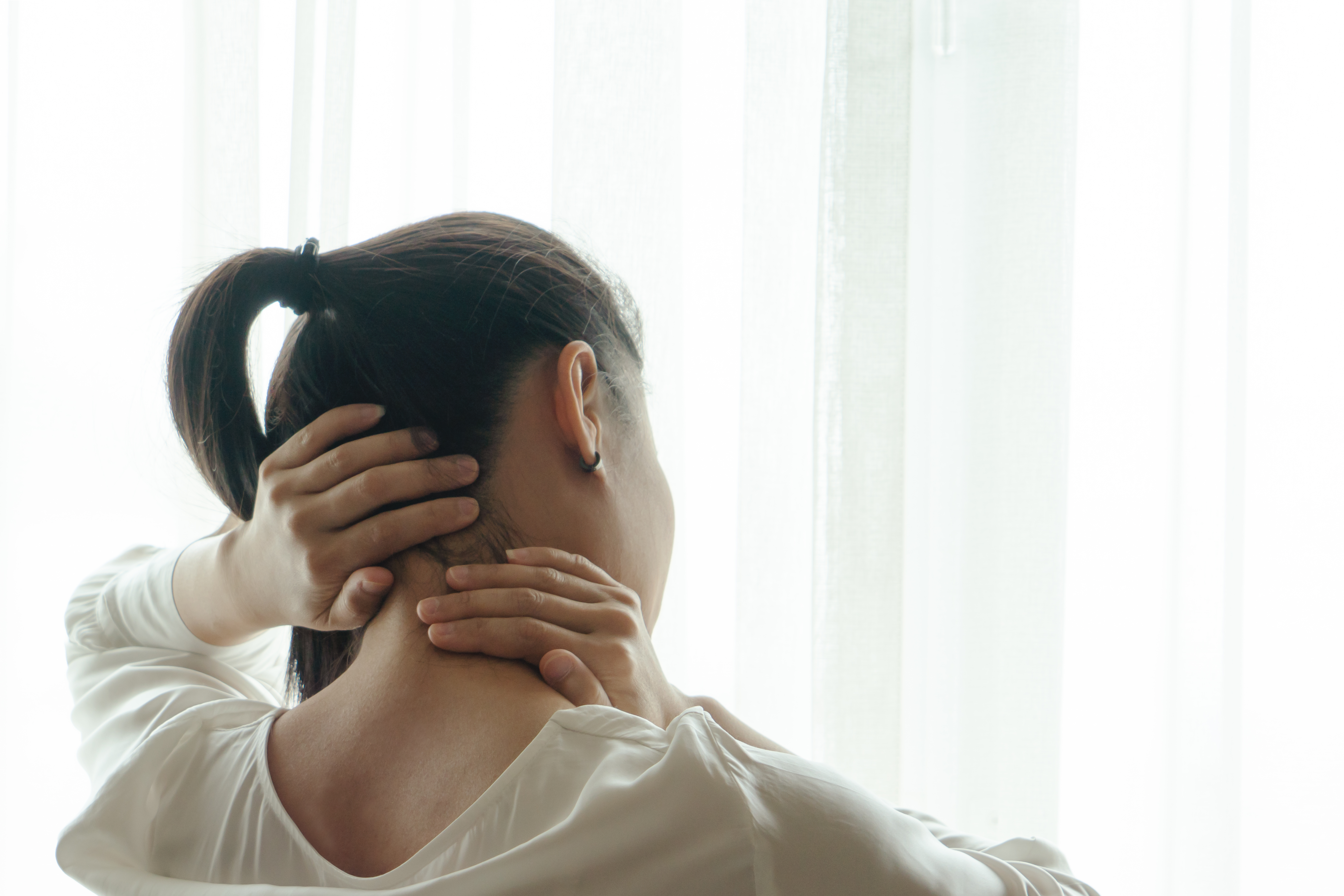 Woman with ponytail grabs the back of her neck and massages it