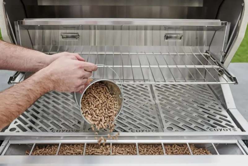 Front view of a man refilling a Coyote wood pellet grill