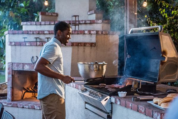 A young man smiling while grilling hamburgers on a grill 