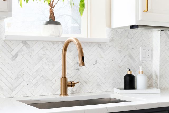 Close view of a modern luxury wet kitchen sink and faucet in a white countertop and backsplash