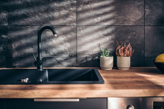 Close view of a luxury black sink and faucet in wooden countertops with a dark stone backsplash