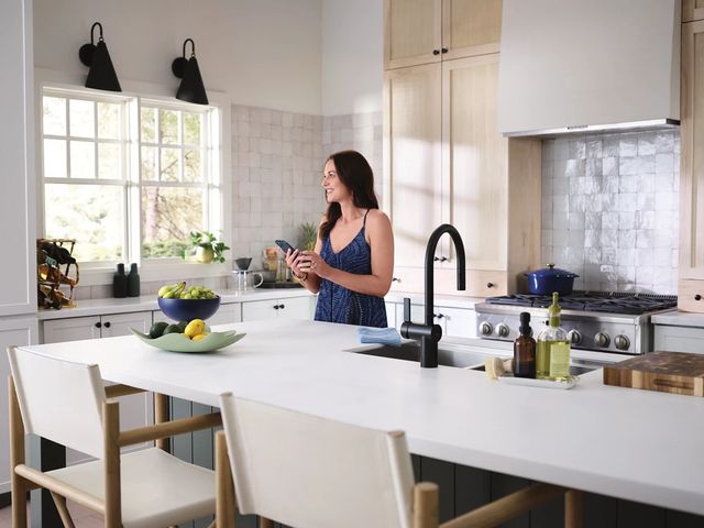 Front view of a woman on her phone in her modern kitchen next to a Moan Faucet