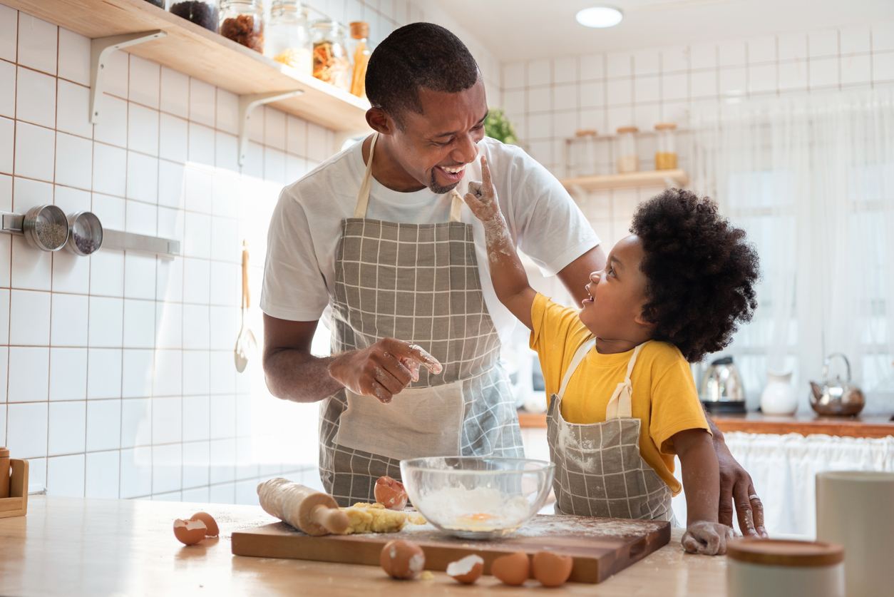 Son boops his father's nose while they bake cookies in a bright kitchen