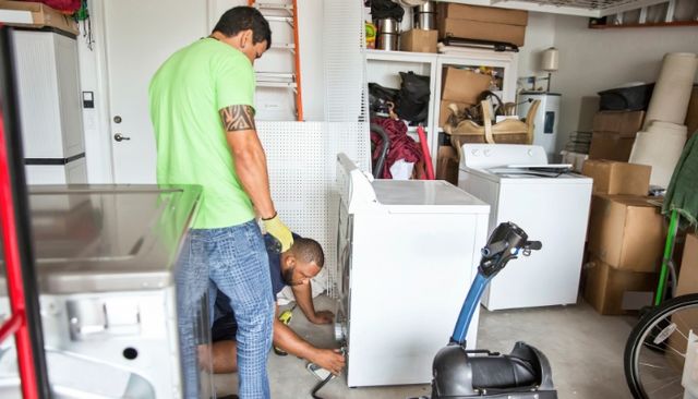 View of two men servicing a washing machine in a garage