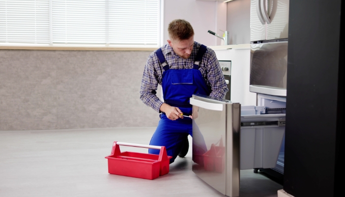 An appliance technician is checking out the freezer on a bottom-freezer fridge