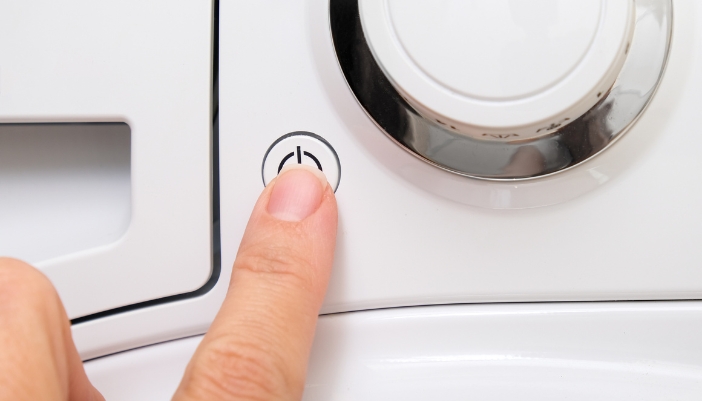 Closeup of someone pushing the power button on washer to help reset it