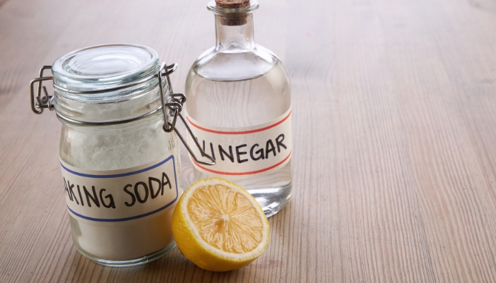 A container of vinegar, baking soda, and half a lemon sit on a wooden surface.