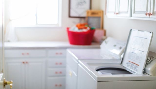 side view of a modern laundry room with an opened top load washer in the front, and the background blurred out